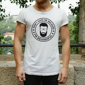 May include: White t-shirt with a black and white graphic of a man with a beard and the text "Don't hate me because I'm beardful."