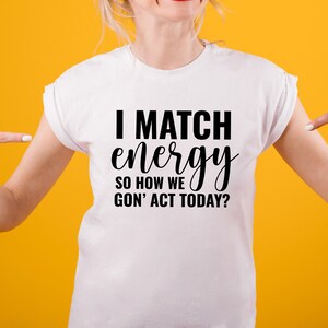 May include: White t-shirt with black text that reads "I match energy so how we gon' act today?"