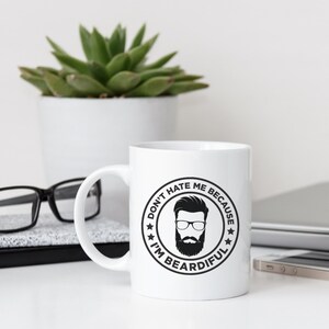 May include: White ceramic coffee mug with a black and white graphic of a man with a beard and the text "Don't hate me because I'm Beardifull".