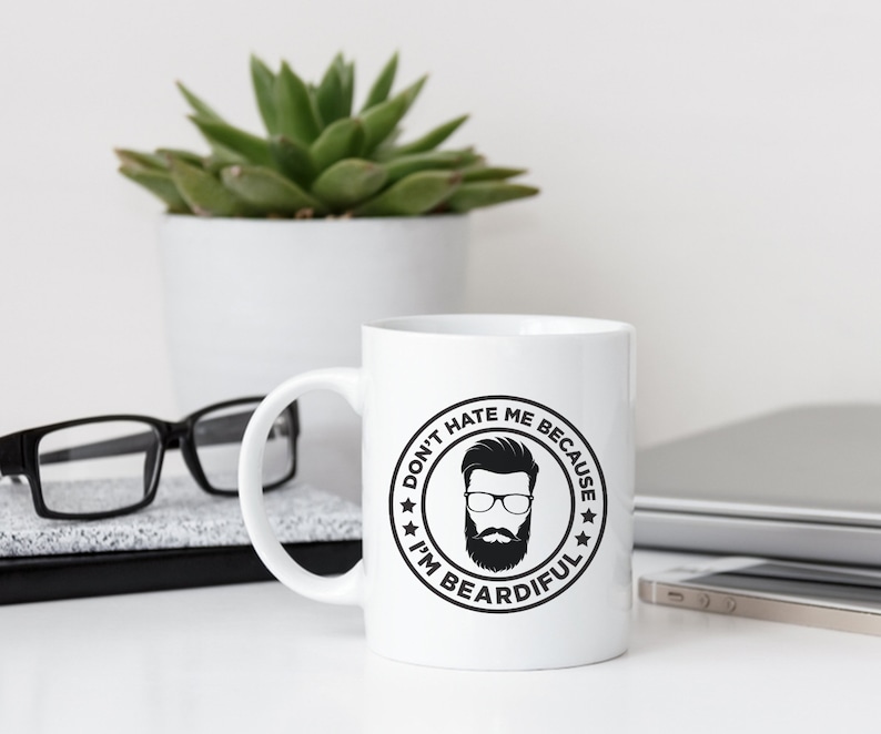 May include: White ceramic coffee mug with a black and white graphic of a man with a beard and the text "Don't hate me because I'm Beardifull".