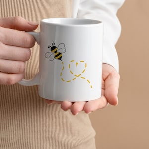 May include: White ceramic mug with a black and yellow bee illustration and a yellow dotted line design. The bee is flying and leaving a dotted line behind it.