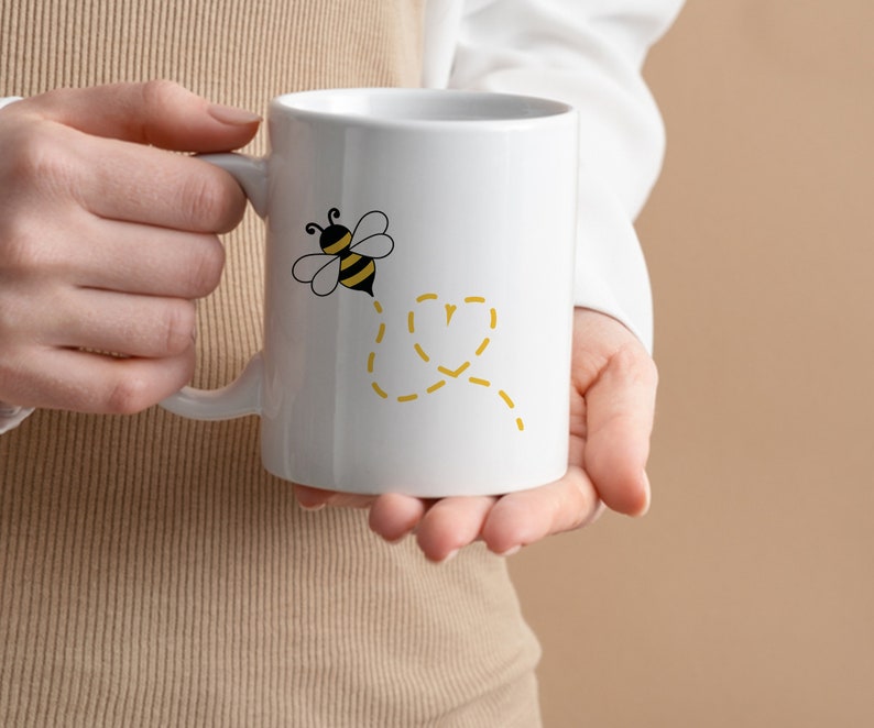 May include: White ceramic mug with a black and yellow bee illustration and a yellow dotted line design. The bee is flying and leaving a dotted line behind it.