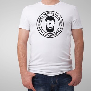 May include: White t-shirt with a black and white graphic of a man with a beard and glasses. The graphic is inside a circle with the text "Don't hate me because I'm beardful".
