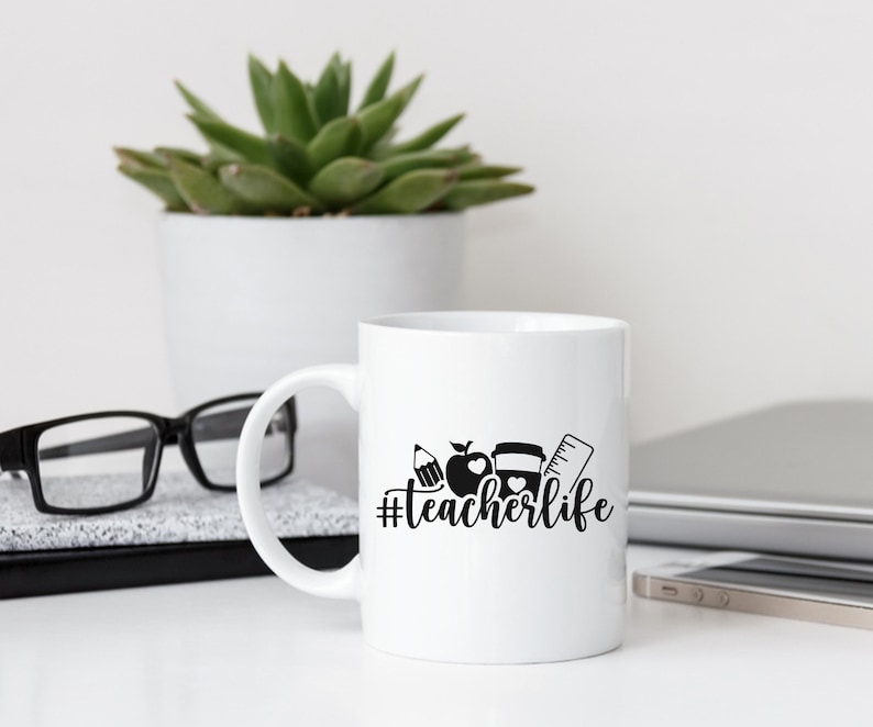 May include: White ceramic coffee mug with a black design of a pencil, apple, coffee cup, and ruler with the text "#teacherlife" printed on the side.