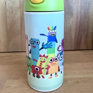 May include: A colorful water bottle featuring cartoon characters. The bottle has a blue, green, and yellow lid. The body of the bottle is light blue and decorated with various cartoon characters. The bottle is cylindrical and appears to be made of metal.