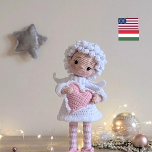 May include: A handmade crochet angel doll, holding a pink heart. The doll has white hair, a white dress, and pink striped legs with matching shoes. Decorative elements include a silver star and Christmas ornaments.