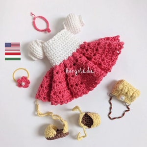 May include: A crocheted doll outfit with a white and pink dress, a yellow purse, a pair of yellow shoes, and a pink flower hair clip. The outfit is handmade and has the text "Horgoláda" on the dress.