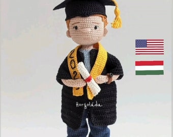 Könnte beinhalten: Eine gehäkelte Abschluss-Puppe, die eine schwarze Mütze und Robe trägt und ein Diplom hält. Die Puppe hat rote Haare und trägt eine blaue Jeans und weiße Turnschuhe. Die Puppe steht auf einem weißen Hintergrund. Der Text "Horgoláda" ist auf der Robe der Puppe sichtbar.