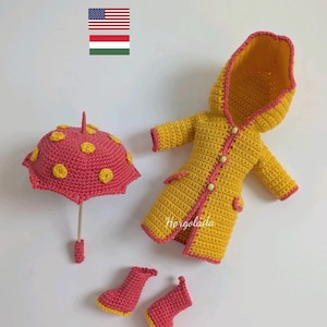 Könnte beinhalten: Ein gehäkelter Regenmantel, Regenschirm und Stiefel in Gelb und Rosa. Der Regenmantel hat eine Kapuze und ist mit Rosa eingefasst. Der Regenschirm hat ein rosafarbenes Dach mit gelben Punkten. Die Stiefel sind rosa mit gelbem Besatz.