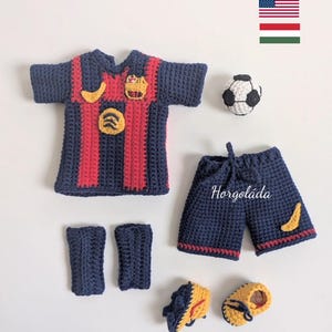 May include: Crocheted soccer uniform set in navy blue and red, including a jersey, shorts, socks, shoes, and a soccer ball. The jersey has red stripes and yellow accents. The shorts have the text "Horgoláda".
