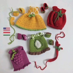 May include: A set of crocheted doll clothes featuring various fruits. The set includes a yellow orange dress, a red tomato dress, a green kiwi dress, a purple grape dress, and a red strawberry dress. The clothes are handmade and feature intricate details.