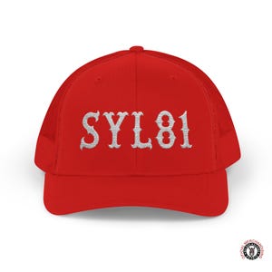 Op de afbeelding: Een rode truckerpet met witte geborduurde letters "SYL81". De pet heeft een mesh achterkant en een gebogen klep. De pet is felrood van kleur.