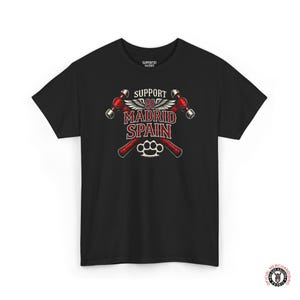 Może przedstawiać: Czarna koszulka z graficznym wzorem. Wzór zawiera napis "SUPPORT 81 MADRID SPAIN" w kolorze czerwono-białym, skrzyżowane młoty, skrzydła i wizerunek kastetu.