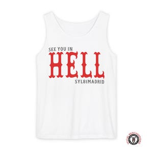 Op de afbeelding: Witte tanktop met de rode tekst "SEE YOU IN HELL" in gestileerde letters. Onder het woord "HELL" staat de tekst "SYL81MADRID". De tanktop heeft een ronde halslijn en is mouwloos. Een klein logo is rechtsonder zichtbaar.