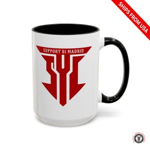 May include: White ceramic mug with a black interior and handle. The mug features a red graphic with the text "SUPPORT 81 MADRID" and "SYI". The mug is a standard size for coffee or tea.
