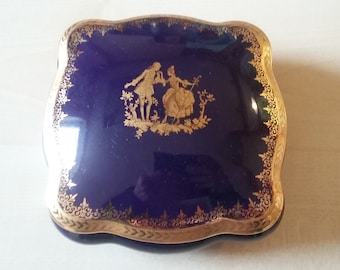 May include: A small, square, cobalt blue trinket box with a gold trim and a gold design of a couple dancing in a garden.