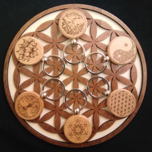 Peut inclure: Un cercle en bois avec un motif de fleur de vie et six porte-clés en bois avec des motifs différents. Les porte-clés présentent un arbre de vie, un yin yang, une fleur de vie, un motif géométrique, une fleur et un motif géométrique.