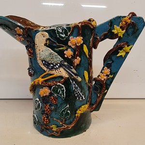 Könnte beinhalten: Eine blaue Keramikkanne mit Vogel- und Blumendesign. Die Kanne hat einen braunen Henkel und einen breiten Ausguss.