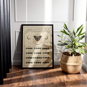 May include: A black framed poster with a beige background featuring a lunar calendar for 2025. The calendar shows the phases of the moon for each month of the year. The poster also features a butterfly illustration and the text "LUNAR CALENDAR 2025 NORTHERN HEMISPHERE".