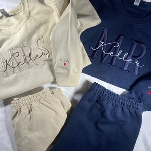 May include: Two matching sets of cream and navy blue sweatshirts and sweatpants with embroidered text. The sweatshirts have "MRS Keller" and "MR Keller" embroidered on them. The date "2.4.24" is embroidered on the sleeves of both sweatshirts.