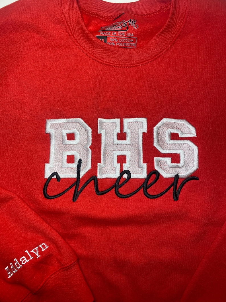 May include: Red sweatshirt with white and gray embroidered lettering that says "BHS cheer" and a smaller white embroidered name "Addalyn" on the sleeve.