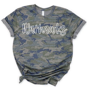 May include: A camouflage print t-shirt with the word "Warhawks" written in white outlined text.