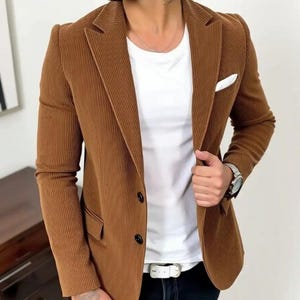 Puede incluir: Una blazer de pana marr&oacute;n con cierre de dos botones, bolsillo en el pecho y solapa con muescas. La blazer se lleva sobre una camiseta blanca y unos vaqueros negros. La imagen incluye el texto "ERA FASHION SHOP".