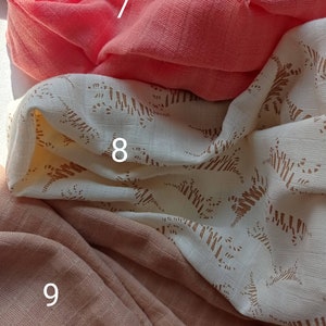 May include: Close-up of three different fabrics. The top fabric is a vibrant coral color, the middle fabric is off-white with a brown pattern, and the bottom fabric is a muted peach color. The fabrics are soft and textured.