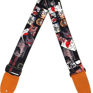 Puede incluir: Correa de guitarra negra con un collage de logotipos de bandas y arte de álbumes, incluyendo The Beatles, Green Day y Jimi Hendrix. Tiene extremos de cuero marrón y una hebilla negra ajustable.