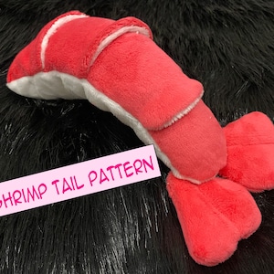 May include: A plush pink and white shrimp tail toy with the text "Shrimp Tail Pattern" on a black background.