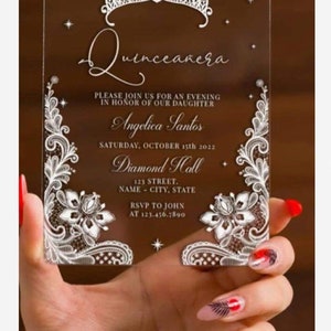 May include: A clear acrylic Quinceanera invitation with a white lace design and a crown at the top. The invitation reads "Quinceanera" and includes the text "Please join us for an evening in honor of our daughter Angelica Santos Saturday, October 15th 2022 Diamond Hall 123 Street, Name - City, State RSVP to John at 123.456.7890".