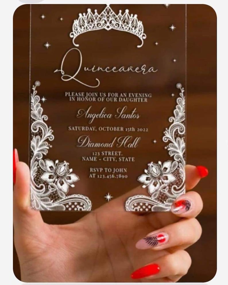 May include: A clear acrylic Quinceanera invitation with a white lace design and a crown at the top. The invitation reads "Quinceanera" and includes the text "Please join us for an evening in honor of our daughter Angelica Santos Saturday, October 15th 2022 Diamond Hall 123 Street, Name - City, State RSVP to John at 123.456.7890".