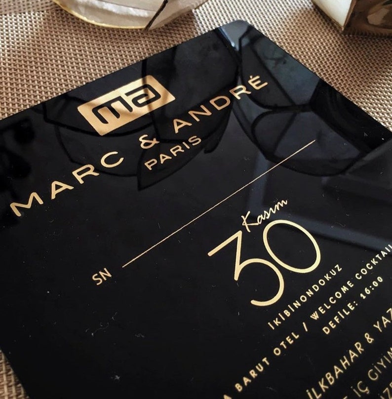 May include: Black and gold invitation card with the text "ma MARC & ANDR&Eacute; PARIS" and "Kasım 30" in gold lettering. The text "İKİBİNONDOKUZ BARUT OTEL / WELCOME COCKTAIL DEFİLE: 16:00 İLKBAHAR & YAZ İ&Ccedil; GİYİN Z" is also in gold lettering.