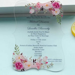 May include: Clear acrylic wedding invitation with pink and white floral design. The invitation reads "On This Special Day When Two Hearts Become One Mildred Danvers & Lascelles Barnaby Joyfully Invite You To Share In Their Happiness As They Unite In Marriage On Friday 17 July 2020 14:00 At Forest of Arden Marriott Hotel & Country Club Arden Suite Maxstoke Lane Meriden Coventry CV7 7HR RSVP: 07828904923 Monetary Gifts Only"