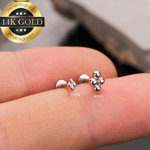 Può includere: Due gioielli per il corpo in oro 14K. Un pezzo è un design a croce da 2 mm e l'altro è un design a grappolo da 4 mm. I gioielli sono mostrati su un dito. L'immagine include il testo "14K GOLD" e "Premium Quality".