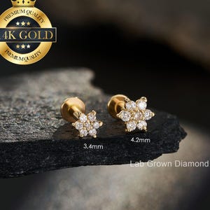 May include: Two gold flower-shaped earrings with clear gemstones. The earrings are 3.4mm and 4.2mm in size. The image includes the text "14K GOLD" and "Lab Grown Diamond". The earrings are on a dark gray surface.