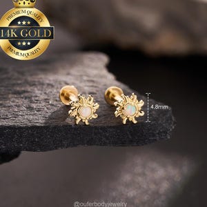 May include: Two 14K gold stud earrings featuring a sunburst design with a central round opal stone. The earrings have a post back and a diameter of 4.8mm as indicated by the measurement graphic. A gold seal states 14K GOLD PREMIUM QUALITY.