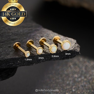 May include: Four gold-colored, flat-back earrings with white opal stones, ranging in size from 1.5mm to 3mm. The earrings are displayed on a dark, textured surface. A gold seal with the text "Premium Quality" and "14K Gold" is in the upper left corner.