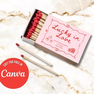 May include: A pink matchbox with the words "Lucky in Love" in red script, with dice and gift illustrations. The box is open, revealing red-tipped matches. Two loose matches lie beside the box. The text "Edit for free in Canva" is in a red circle.