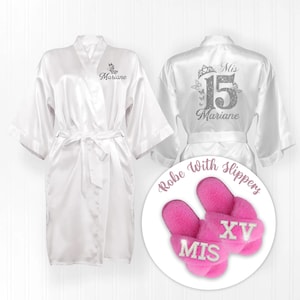 May include: White satin robe with silver embroidery that says "Mis 15 Marianne" on the back and "Marianne" on the front. The robe comes with a pair of pink fuzzy slippers that say "Mis XV" in silver glitter.
