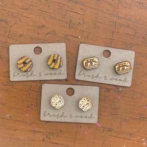 May include: Three sets of wooden earrings on cards. The first set features a brown and yellow striped design. The second set features a rectangular design with the text "Girl Scout S'mores". The third set features a brown and white design with a wave pattern.
