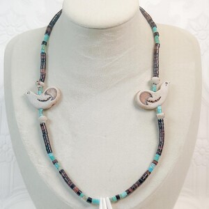 May include: A necklace with bird-shaped pendants and a central pendant of three white pieces. The necklace features turquoise, brown, and black beads. The bird pendants are off-white with etched details.