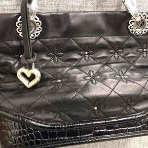 Pu&ograve; includere: Borsa tote in pelle nera trapuntata con dettagli in argento e un ciondolo a forma di cuore. La borsa ha un fondo in pelle con effetto coccodrilo.