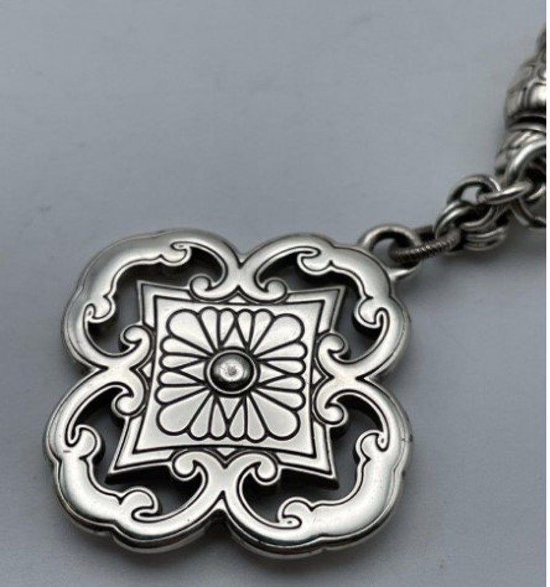 May include: A silver pendant with a detailed floral design. The pendant is attached to a silver chain.