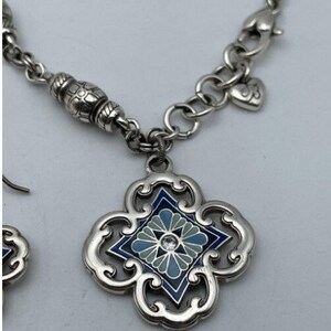 May include: A silver necklace and earrings set with a blue and white enamel pendant featuring a floral design. The pendant is surrounded by a silver filigree frame.