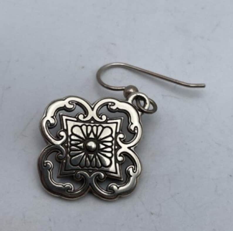 May include: Silver filigree earring with a square design featuring a detailed floral pattern.