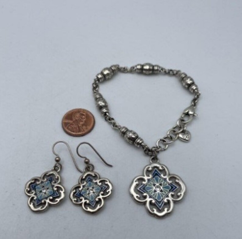 May include: A silver bracelet with a blue and white enamel charm, and matching earrings with the same design. The bracelet has a heart charm and is made of silver beads.