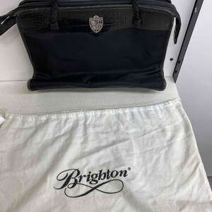 K&ouml;nnte beinhalten: Schwarze Ledertasche mit silbernem Brighton-Logo und einem Staubbeutel mit der Aufschrift "Brighton" in Kursivschrift.