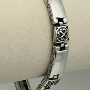 Puede incluir: Una pulsera de plata con una serie de eslabones rectangulares y cuadrados. Los eslabones rectangulares son lisos, mientras que los eslabones cuadrados presentan un dise&ntilde;o decorativo de cruz. La pulsera tiene un patr&oacute;n ornamentado y grabado en los bordes.