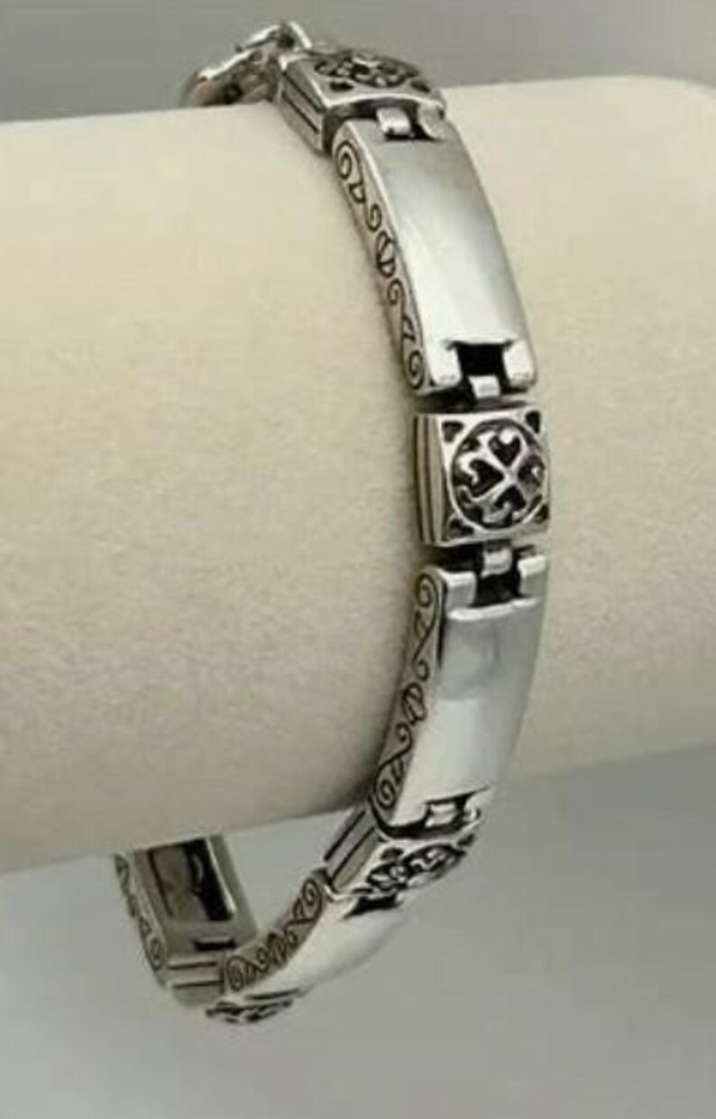 Puede incluir: Una pulsera de plata con una serie de eslabones rectangulares y cuadrados. Los eslabones rectangulares son lisos, mientras que los eslabones cuadrados presentan un dise&ntilde;o decorativo de cruz. La pulsera tiene un patr&oacute;n ornamentado y grabado en los bordes.